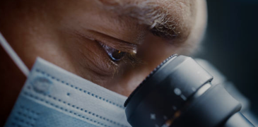 Scientist wearing surgical mask and looking into microscope.png