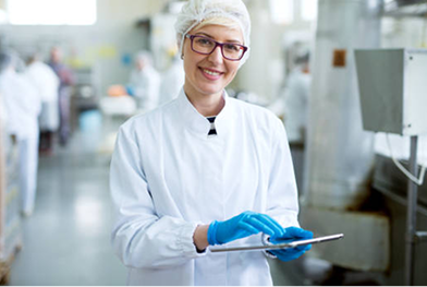 Female worker in sterile cloths holding a tablet and smiling.png