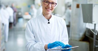 Female worker in sterile cloths holding a tablet and smiling.png