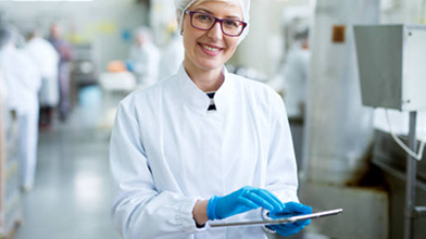 Female worker in sterile cloths holding a tablet and smiling.png